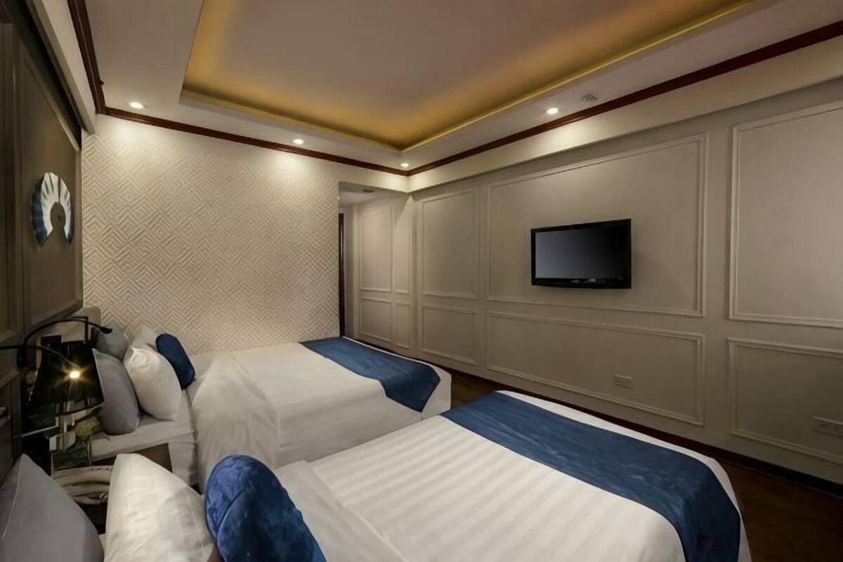 Une chambre d’hôtel avec deux lits, un téléviseur fixé au mur et un papier peint à motifs.