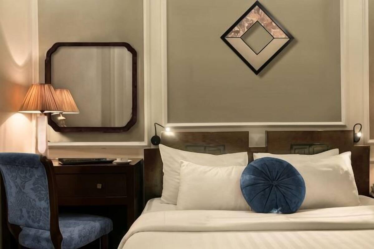Une chambre d’hôtel équipée d’un lit, d’un bureau, d’une chaise, d’une lampe et d’un miroir fixé au mur.