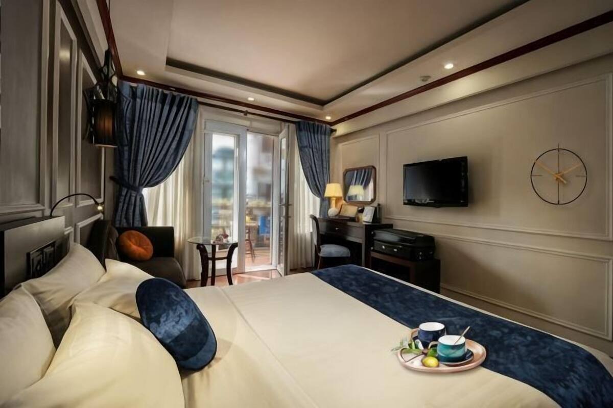 Une chambre d’hôtel avec un grand lit, un bureau, une chaise, une télévision et un balcon avec des rideaux.