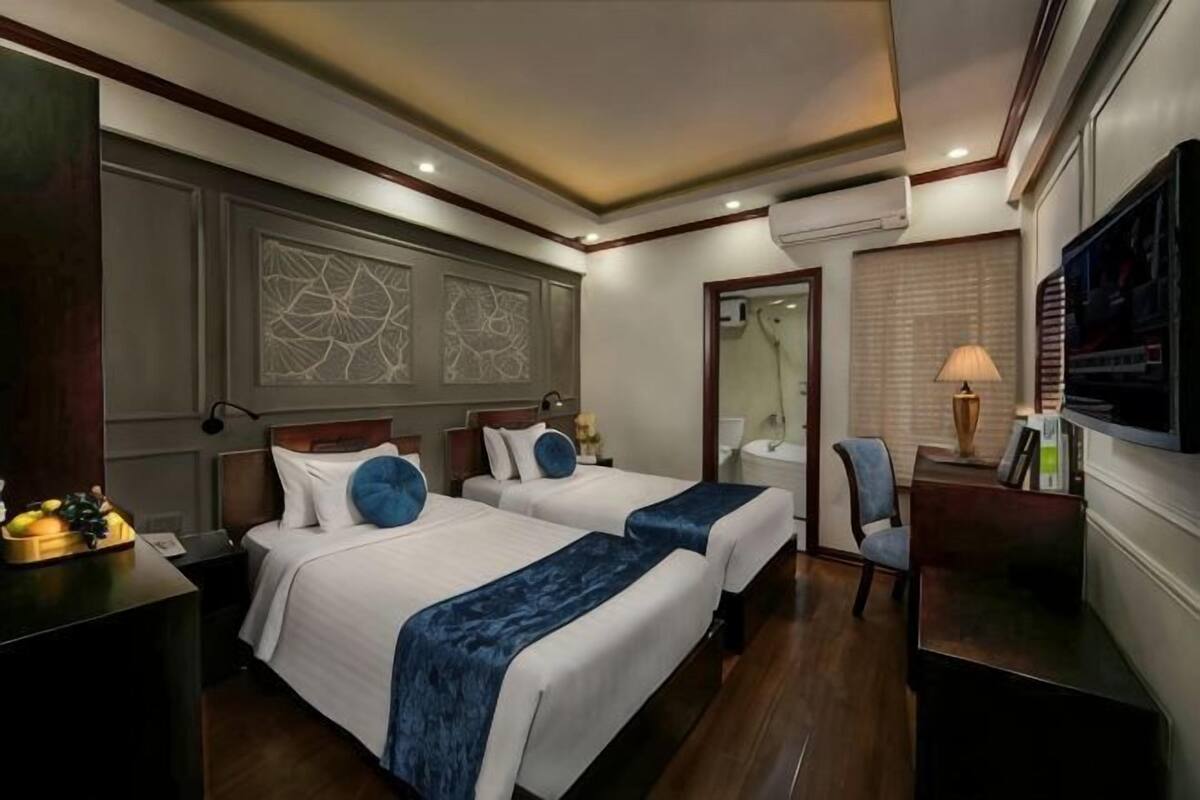 Une chambre d’hôtel avec deux lits, un bureau, une chaise, une télévision et un miroir.