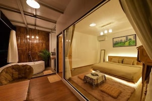 Un dormitorio moderno con una cama grande, un rincón de descanso con una silla y una mesa, y vistas a través de un muro de cristal.