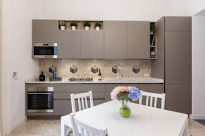 A modern kitchen with built-in appliances, a dining table with chairs, and a vase with flowers. - L'Orchidea al Museo appartament in the center (Naples)