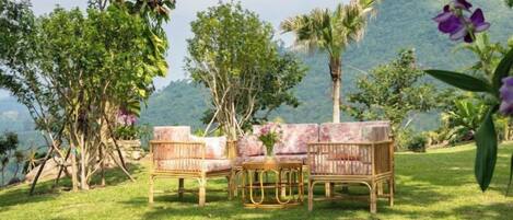 A wicker sofa set on a grassy lawn with a mountainous backdrop.