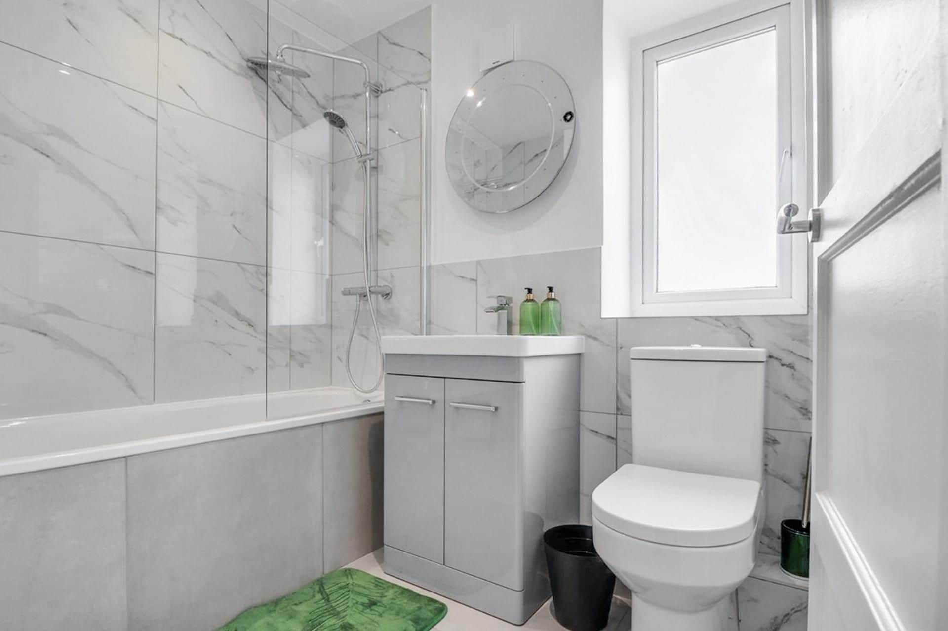 Un baño con ducha, inodoro, lavamanos y espejo.