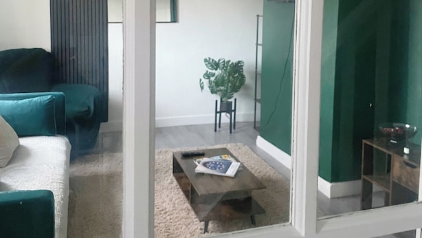 A living room with a teal sofa, a small coffee table with a book, and a potted plant. - Your Home-from-home - Business & Families - 6 Beds (Ilford)