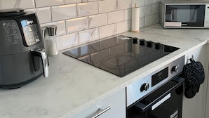 A kitchen with a black induction cooktop, a built-in oven, and a microwave. - Your Home-from-home - Business & Families - 6 Beds (Ilford)