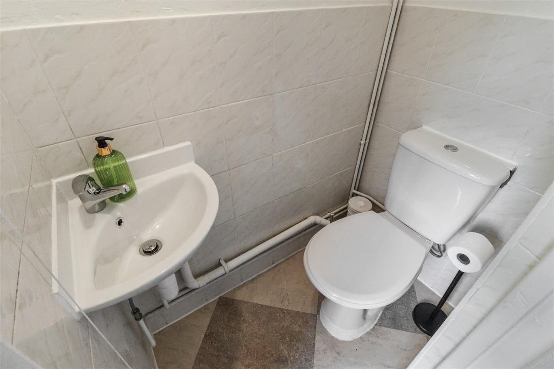 Une salle de bain avec un lavabo blanc, des toilettes et un flacon de savon vert.