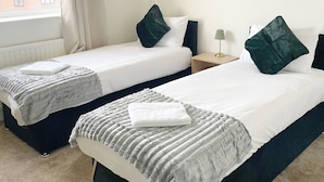 Two single beds with dark headboards, white linens, and green pillows. There is a small bedside table with a lamp and a window with curtains. - Your Home-from-home - Business & Families - 6 Beds (Ilford)