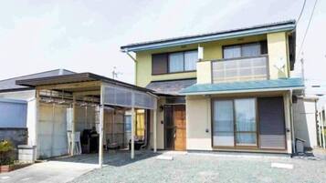 A two-story residential building with a covered carport, a front porch, and a small garden area.