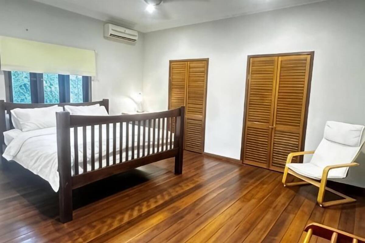 Une chambre Ă coucher avec un lit en bois, une chaise blanche et des armoires en bois.