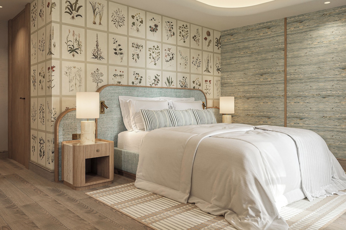 Ein Schlafzimmer mit einem großen Bett, zwei Nachttischen, einem Beistelltisch und einer Wand mit botanischem Wandpapier.