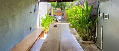 Un sendero estrecho con un banco de madera, plantas en macetas y un colgador de luz.