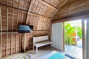 Una habitación con techo de madera, televisor de pantalla plana en la pared, un banco blanco y vista a zonas verdes.