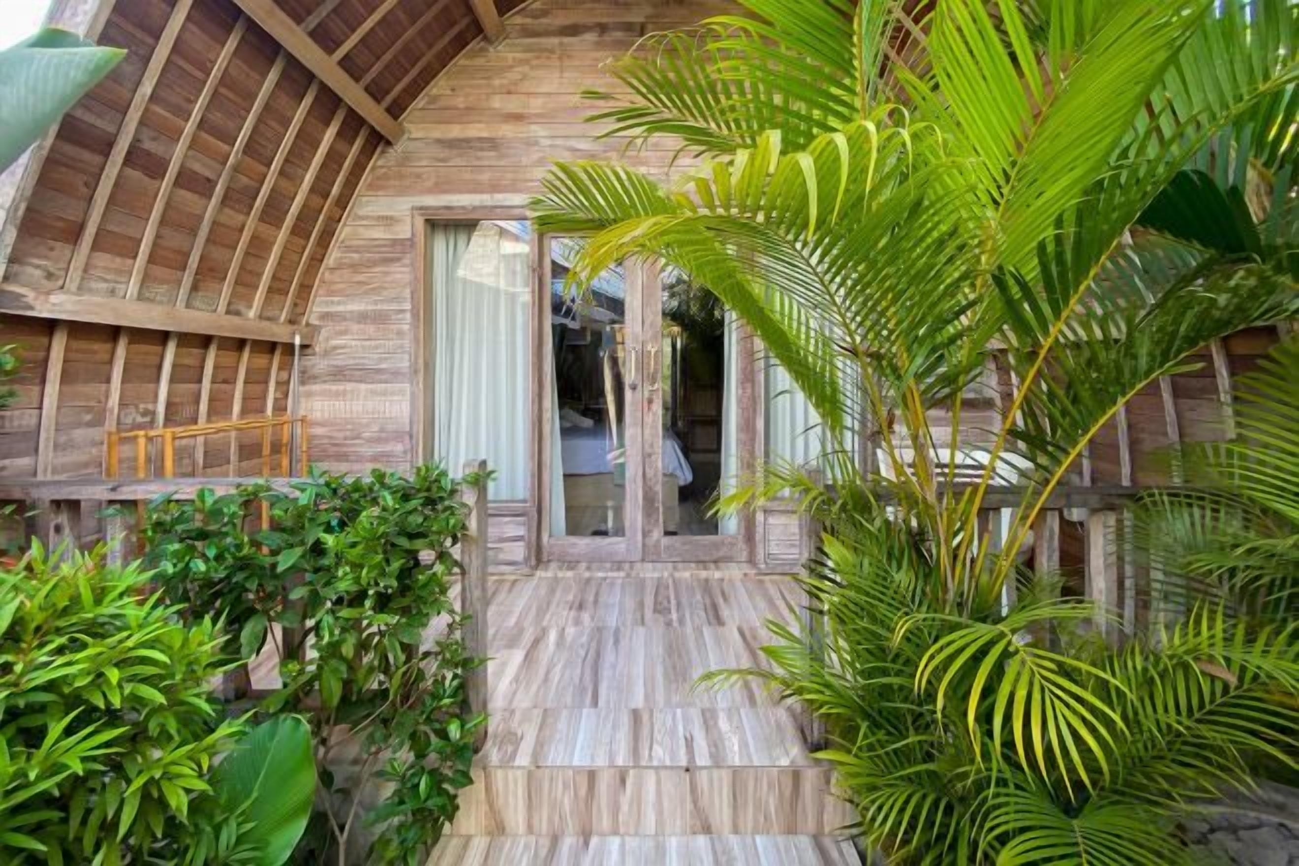 A wooden exterior with a glass door entrance, surrounded by lush greenery.