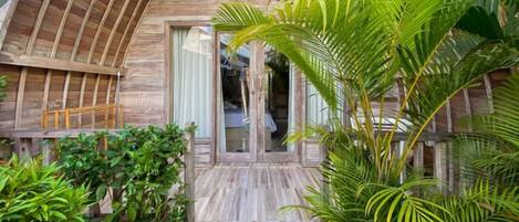 A wooden exterior with a glass door entrance, surrounded by lush greenery.