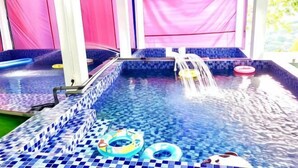 An indoor swimming pool with blue and white mosaic tiles, pink curtains, and inflatable rings. - Penang Dream Banglo (Tanjung Bungah)
