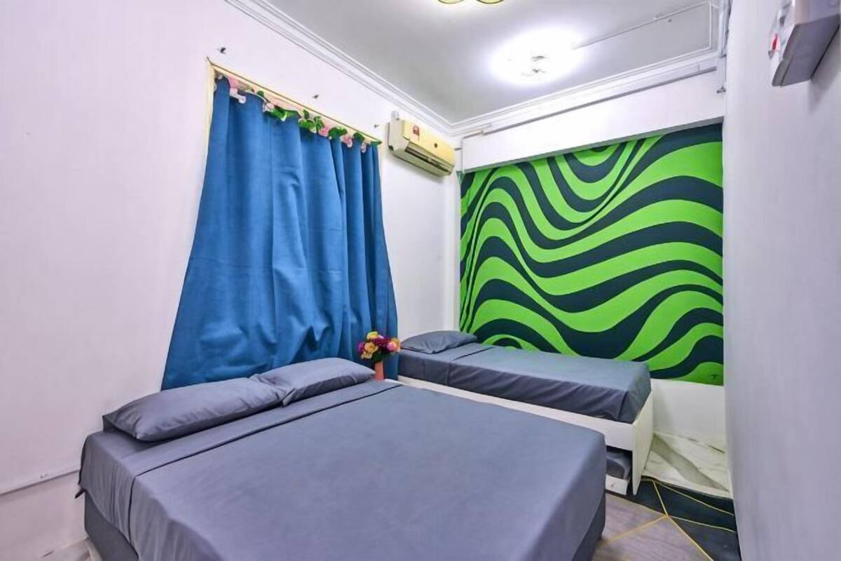 A room with two beds, a curtain, an air conditioning unit, and a wall with a green and black pattern.