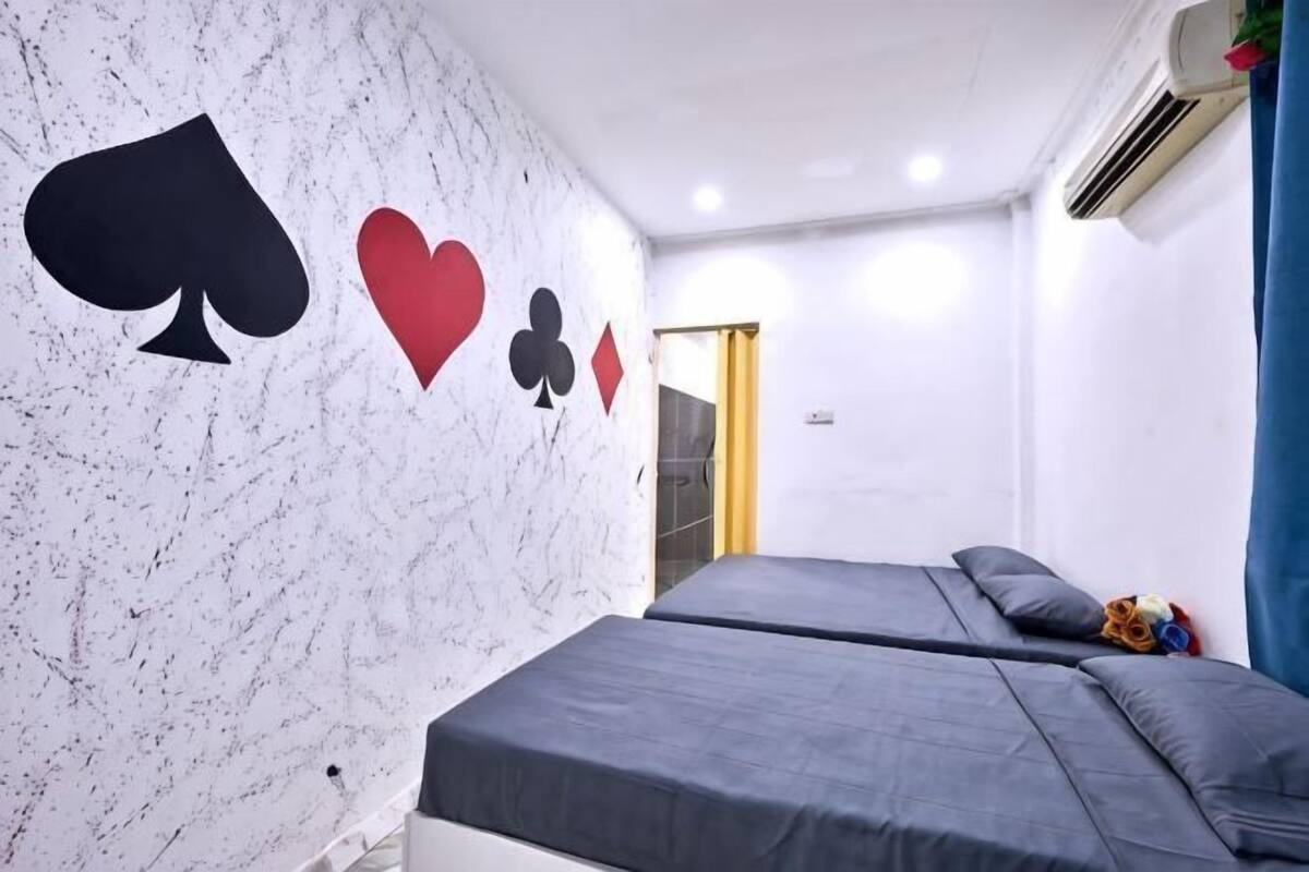 A room with two beds, a wall with playing card symbols, and an air conditioning unit.