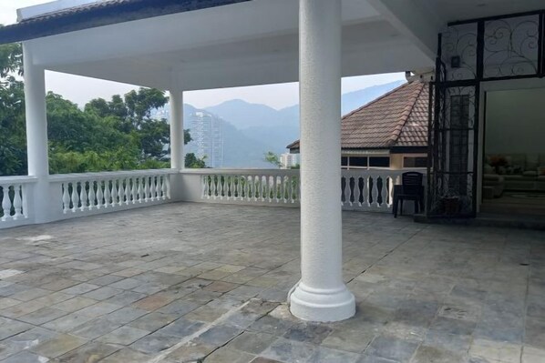A covered outdoor area with stone flooring, white columns, and a view of mountains. - Penang Dream Banglo (Tanjung Bungah)