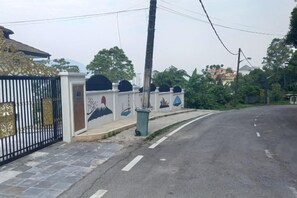 A gated residential area with a curved road, a gated entrance, and a trash bin. - Penang Dream Banglo (Tanjung Bungah)