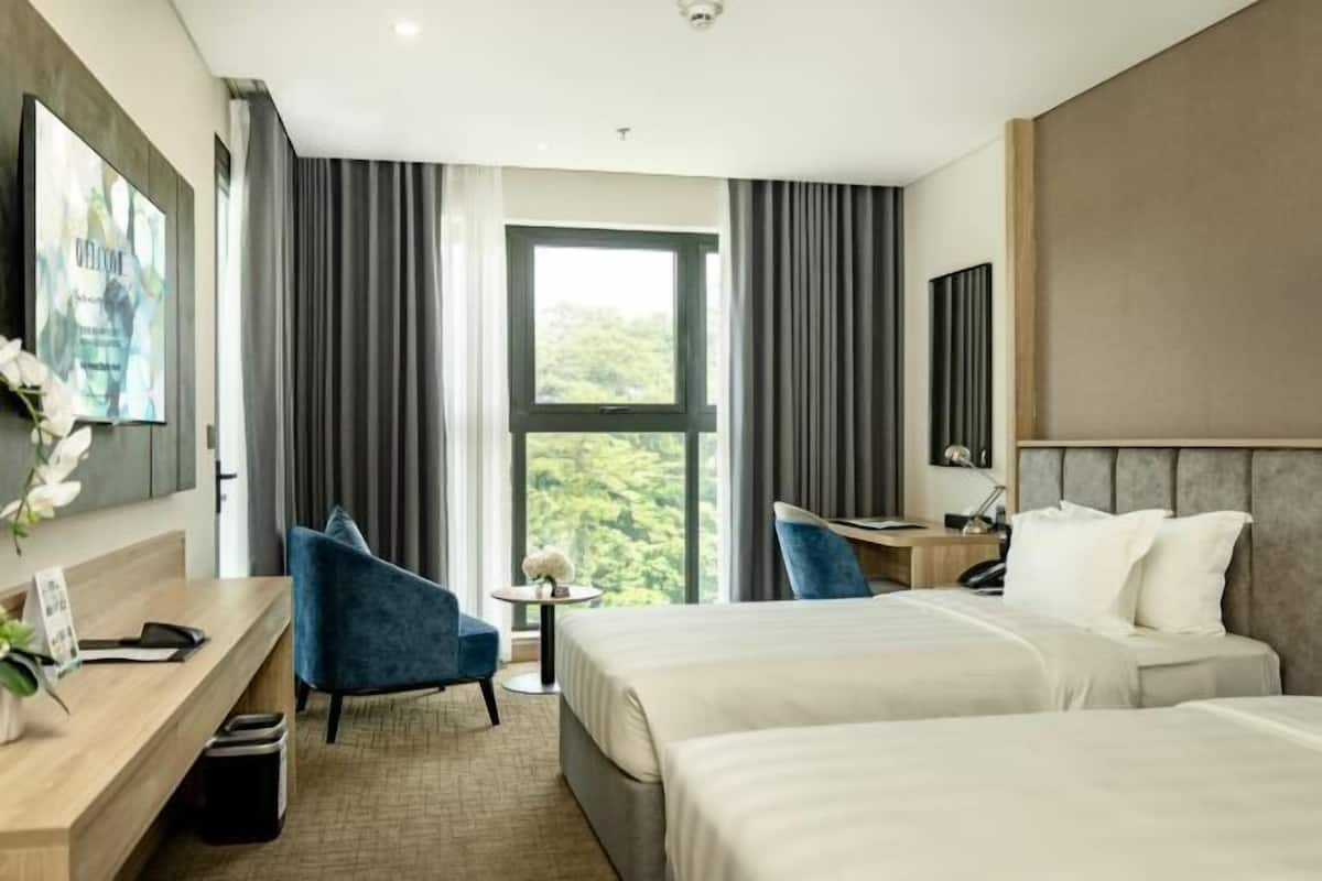 A hotel room with two beds, a desk, a chair, a small table, and a large window with curtains.