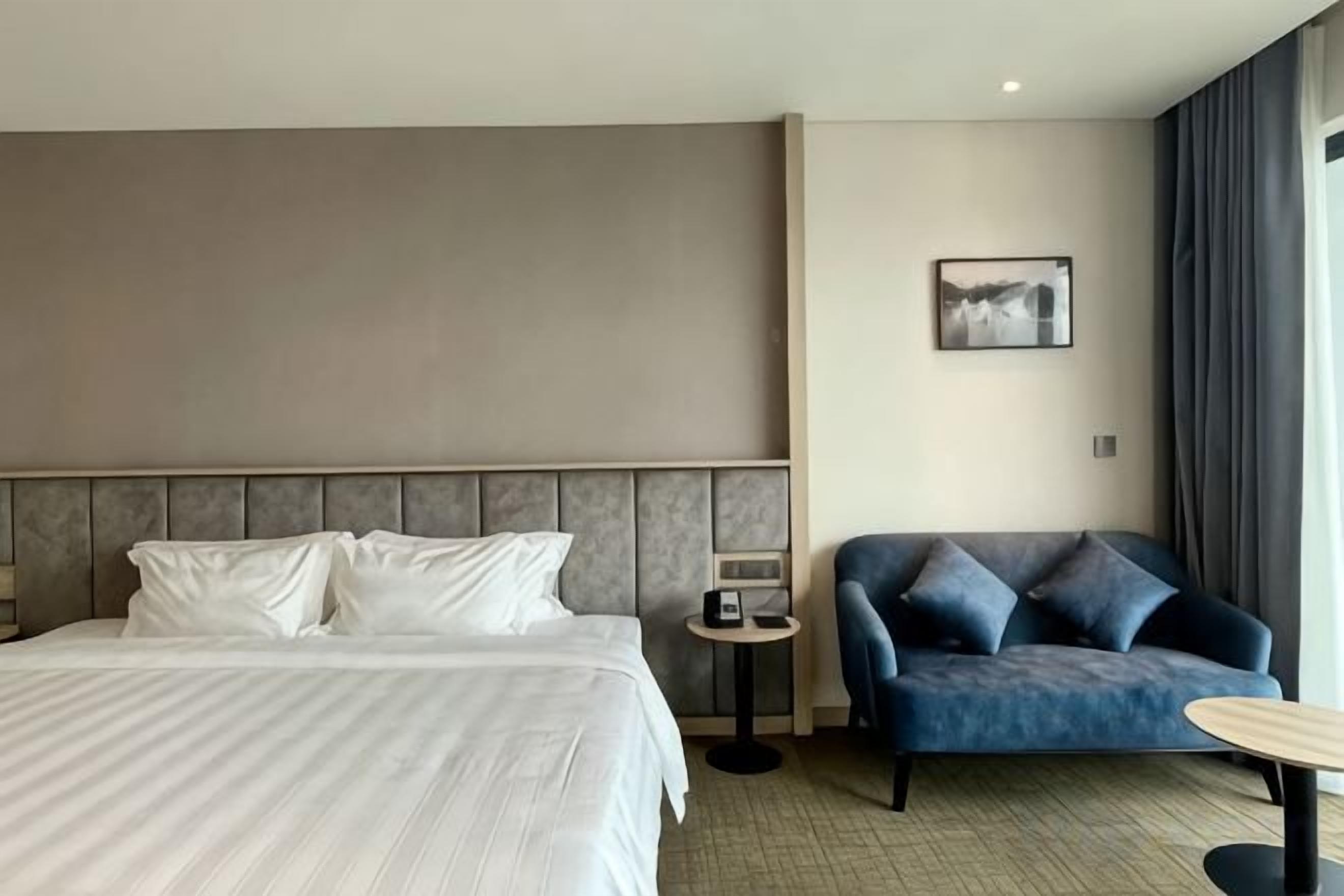 Una habitación de hotel con una cama, un sofá, una mesita y un cuadro colgado en la pared.