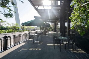 An outdoor patio with tables and chairs, a green umbrella, and a view of the street. - Wyndham Garden Legend Halong (Ha Long)