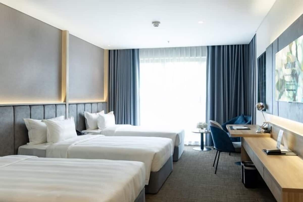 A hotel room with two beds, a desk, a chair, and a window with curtains.
