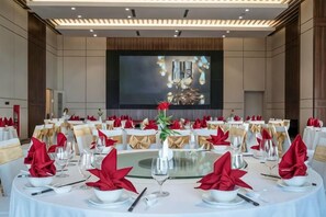 A conference room with round tables set for a meeting, a large screen at the front, and a stage with a podium. - Wyndham Garden Legend Halong (Ha Long)