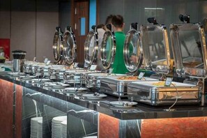A buffet setup with multiple serving stations, each with a glass cover and a variety of food containers. - Wyndham Garden Legend Halong (Ha Long)