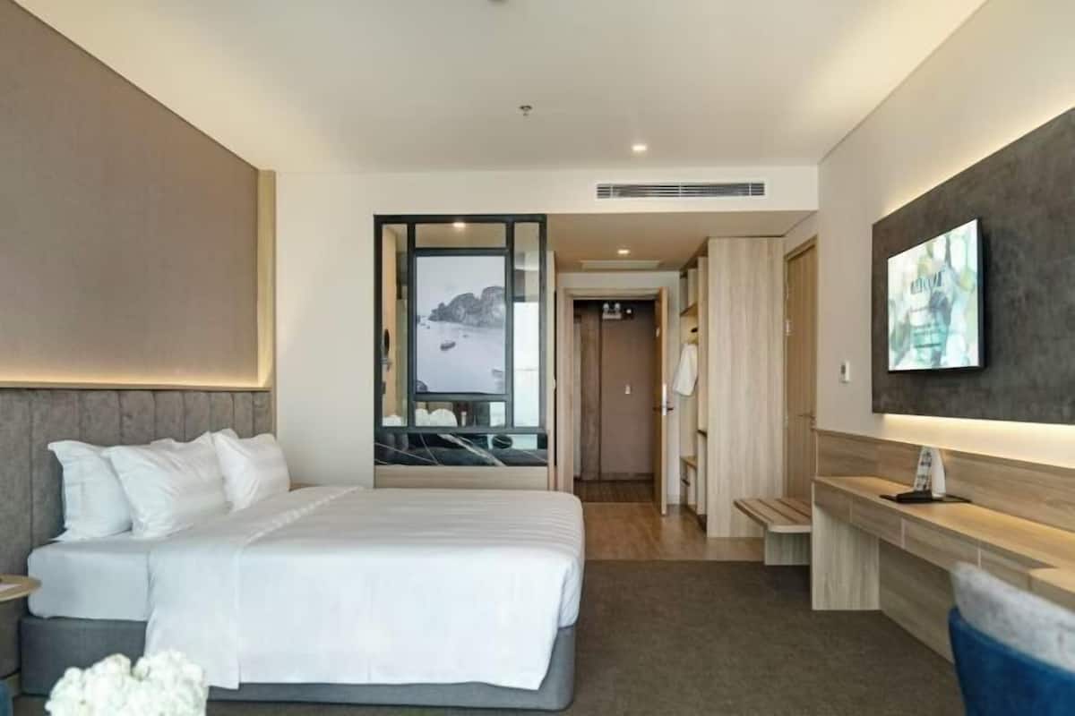 A modern hotel room with a large bed, a desk, and a view of a mountainous landscape through a glass door.