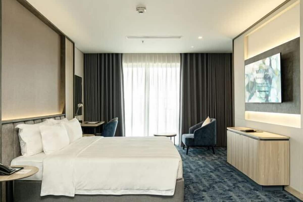 A hotel room with a bed, a desk, a chair, a TV, and a window with curtains.