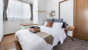 A bedroom with a bed, a bedside table, a nightstand, a window with curtains, a wall-mounted shelf, and a wooden door. - Hatagaya House (Tokyo)