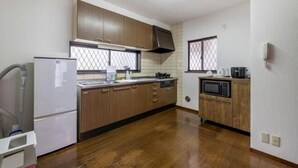 A kitchen with wooden cabinets, a refrigerator, a microwave, and a window with a view. - Hatagaya House (Tokyo)
