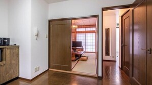 A hallway with a sliding door leading to a living area with a TV, sofa, and tatami mat flooring. - Hatagaya House (Tokyo)