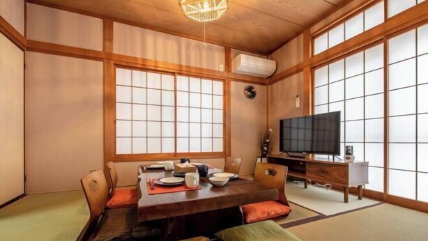 A traditional Japanese-style room with tatami flooring, a low wooden table set for dining, a television, and sliding doors. - Hatagaya House (Tokyo)