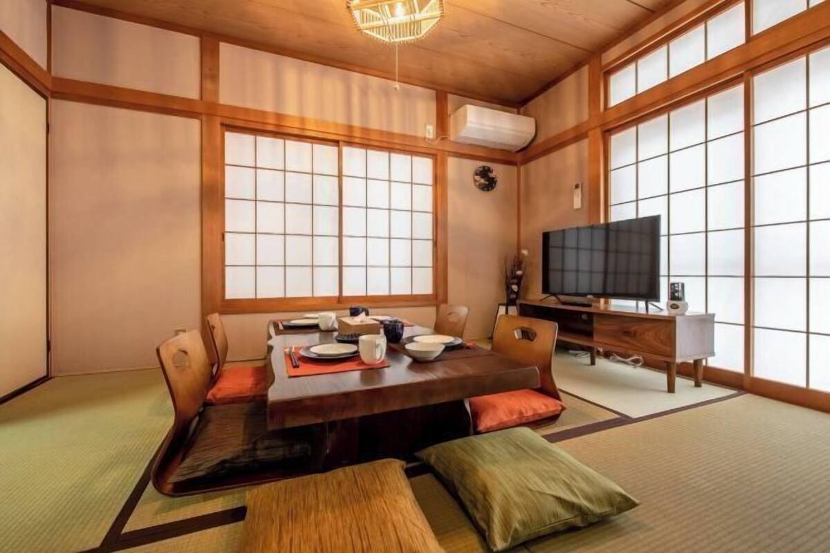 A traditional Japanese-style room with tatami flooring, a low wooden table set for dining, a television, and sliding doors.