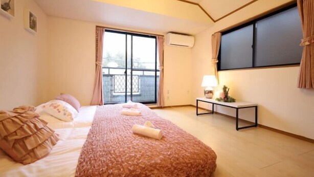 A bedroom with a large bed, a window with curtains, a bedside table with a lamp, and a view of the outside.