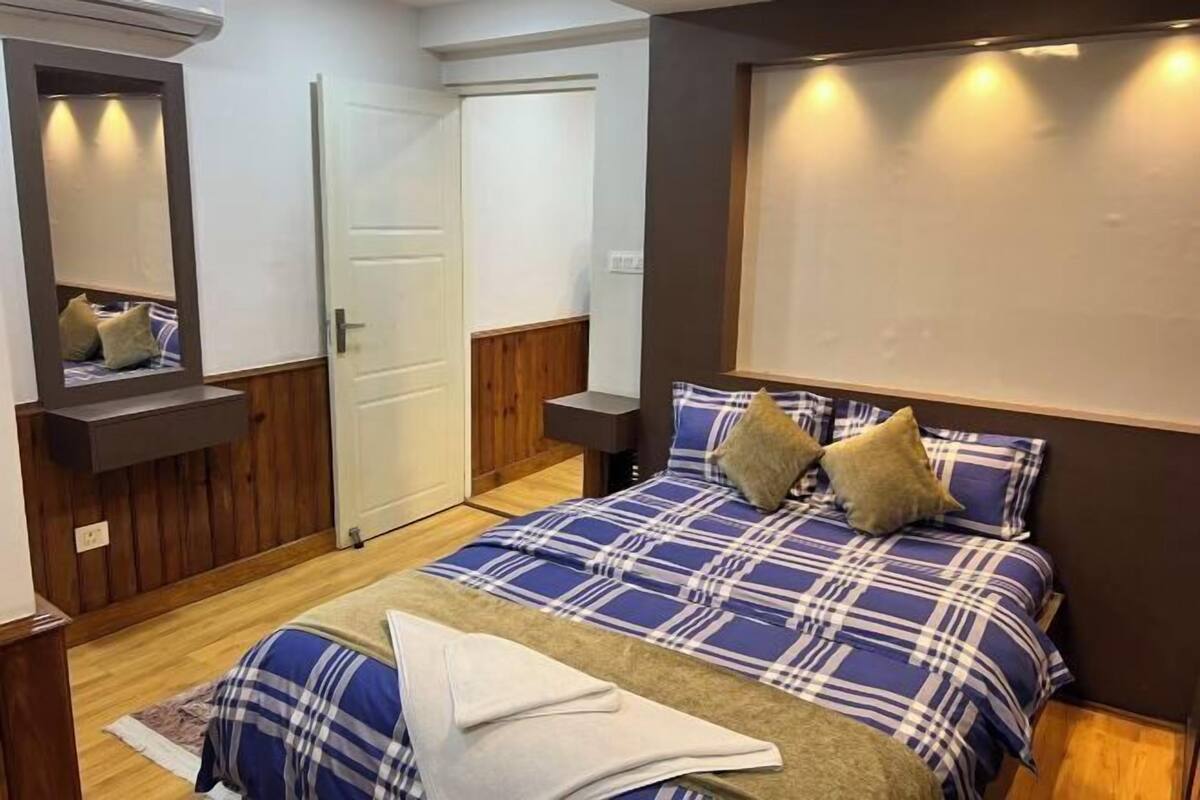 A bedroom with a bed, a mirror, a door, and a wall-mounted light fixture.