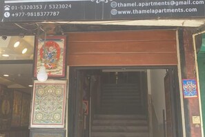 A building entrance with a staircase leading inside, a signboard with contact information, and decorative wall art. - Thamel Holiday Apartments (Kathmandu)