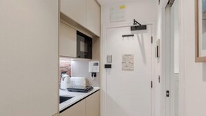 A narrow hallway with a kitchen area on the left, featuring cabinets, a microwave, and a kettle. - Kensington Studio B (Lower level) (London)