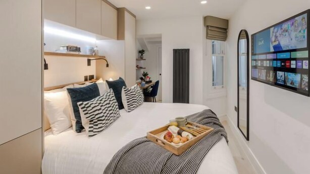 A modern hotel room with a large bed, bedside table, and a wall-mounted TV. - Kensington Studio B (Lower level) (London)