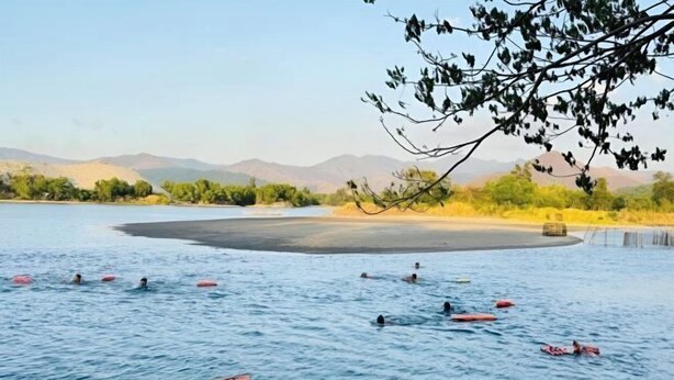 Une zone de baignade où l’on peut voir des personnes dans l’eau, entourée d’un paysage naturel composé de collines et d’arbres.