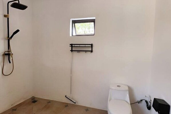 A small bathroom with a toilet, a window, and a shower.
