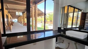 Une chambre d’hôtel dotée d’une grande fenêtre, d’un plan de travail noir et d’un lavabo blanc.