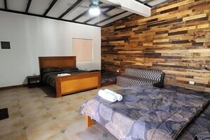 A bedroom with a wooden headboard, a bed with a patterned bedspread, a bedside table, and a nightstand. - Sunset Water Sports Retreat (Cabangan)