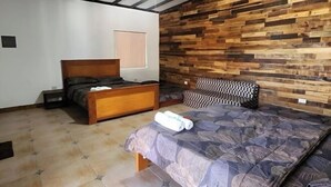 Une chambre à coucher avec une tête de lit en bois, un lit recouvert d’une couvre-lit à motifs, une table de chevet et une fenêtre avec des stores.