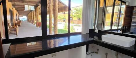A hotel room with a large window, a wooden ceiling, a white sink, and a mirror.