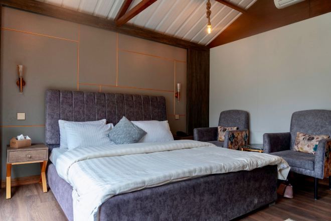 A bedroom with a large bed, two armchairs, a nightstand, and a wooden ceiling.