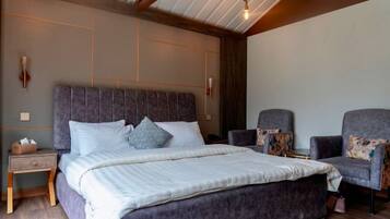 A bedroom with a large bed, two armchairs, a nightstand, and a wooden ceiling.